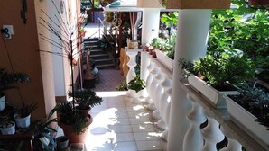 A narrow outdoor corridor with potted plants on both sides, a white balustrade, and a staircase leading to an upper level. - Holiday apartment with terrace, Wi-Fi and air conditioning (Hévíz)