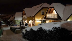 A snow-covered house with a balcony and a lit interior, surrounded by snow.