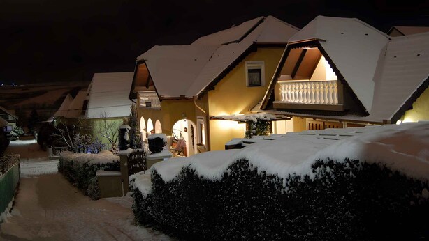 A snow-covered house with a balcony and a lit interior, surrounded by snow. - Holiday apartment with terrace, Wi-Fi and air conditioning (Hévíz)
