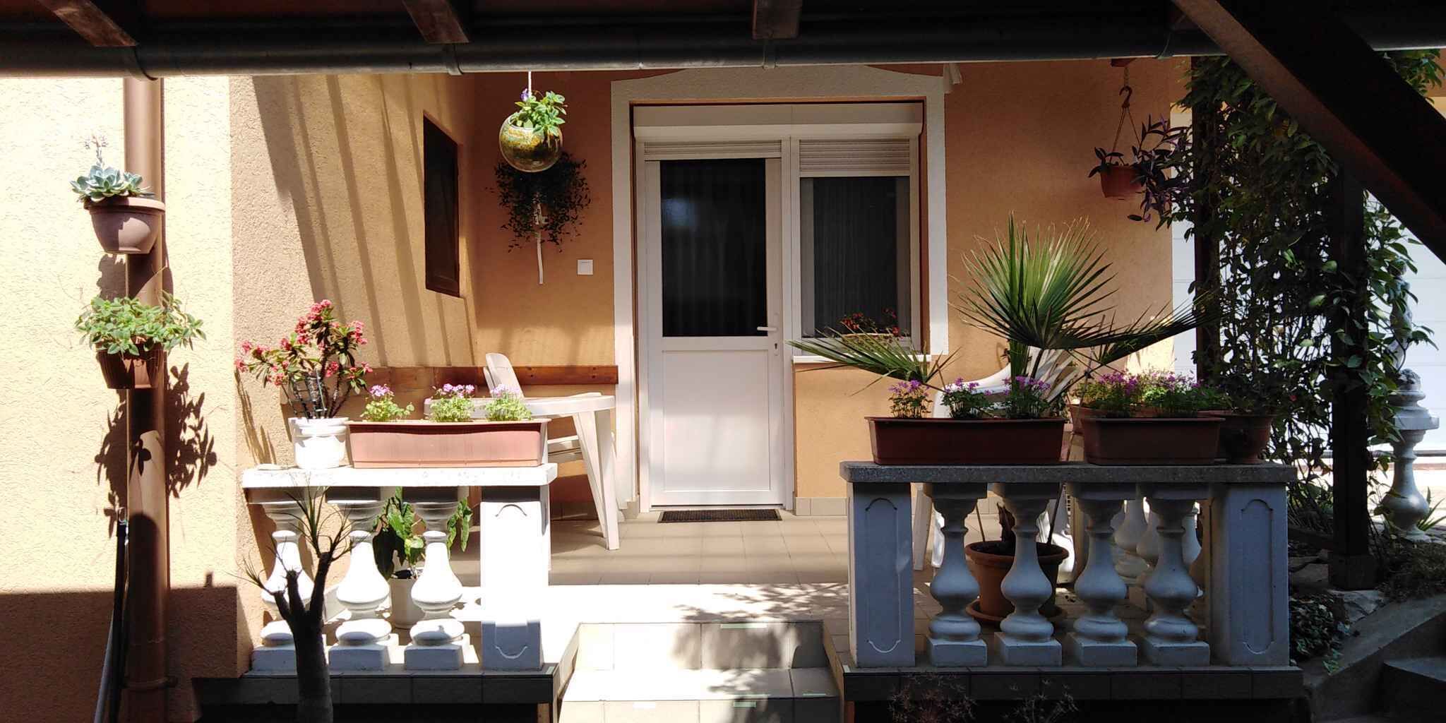 A covered outdoor area with a white door, potted plants, and a small table with chairs.