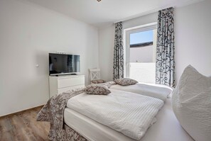Quarto com duas camas, uma televisão e uma janela com cortinas estampadas.