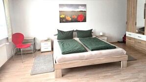 Una camera da letto con un letto, una sedia rossa, un comodino, uno specchio e un quadro appeso al muro.