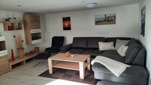 Un soggiorno moderno con un divano grigio, un tavolino in legno, una poltrona nera e un piccolo tavolino laterale con soprammobili.