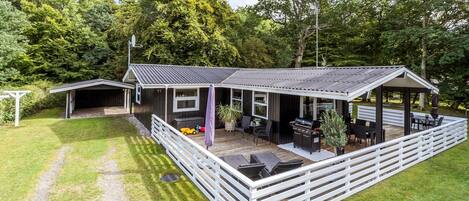 A modern outdoor structure with a covered patio, seating area, and barbecue.