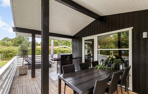 Eine überdachte Terrasse im Freien mit Esstisch und Stühlen, einem Grill und Blick auf Grünflächen.