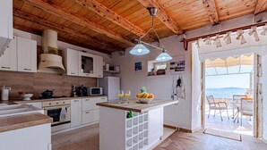 A kitchen with wooden beams, white cabinets, a central island with a fruit bowl, and a view of the sea through an open door. - Awesome home in Mokalo (Mokalo)