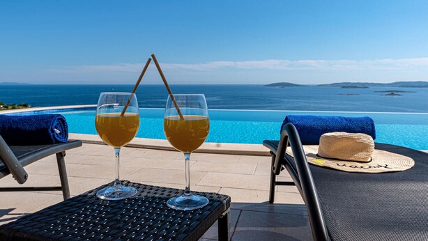A poolside setting with two glasses of a beverage, a straw, and a straw hat on a chair. - Awesome home in Mokalo (Mokalo)