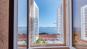 A view from a window with a metal railing, overlooking a body of water and distant land. - Awesome home in Mokalo (Mokalo)