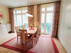 A dining area with a table and chairs, a red rug, and a view through large windows.