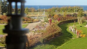 Ein angelegter Garten mit einem Pfad, einem Gewässer und einem Blick auf das Meer in der Ferne.