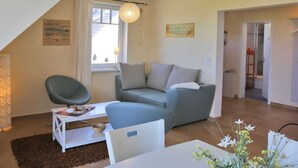 Ein modernes Wohnzimmer mit einer Couch, einem Sessel, einem Tisch und einem Fenster mit Vorhängen.