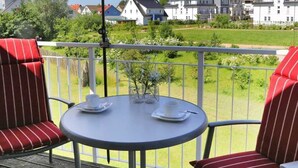 Ein Balkon mit Tisch und Stühlen, einem roten Sonnenschirm und Blick auf Häuser.