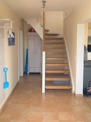 A hallway with a staircase, a white cabinet, and a blue shovel.