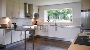 Una cocina moderna con armarios blancos, un refrigerador de acero inoxidable, un microondas y un ventanal con vista a árboles.