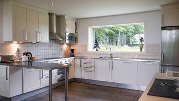 Eine moderne Küche mit weißen Schränken, einem Edelstahlkühlschrank, einer Mikrowelle und einem großen Fenster mit Blick auf Bäume.