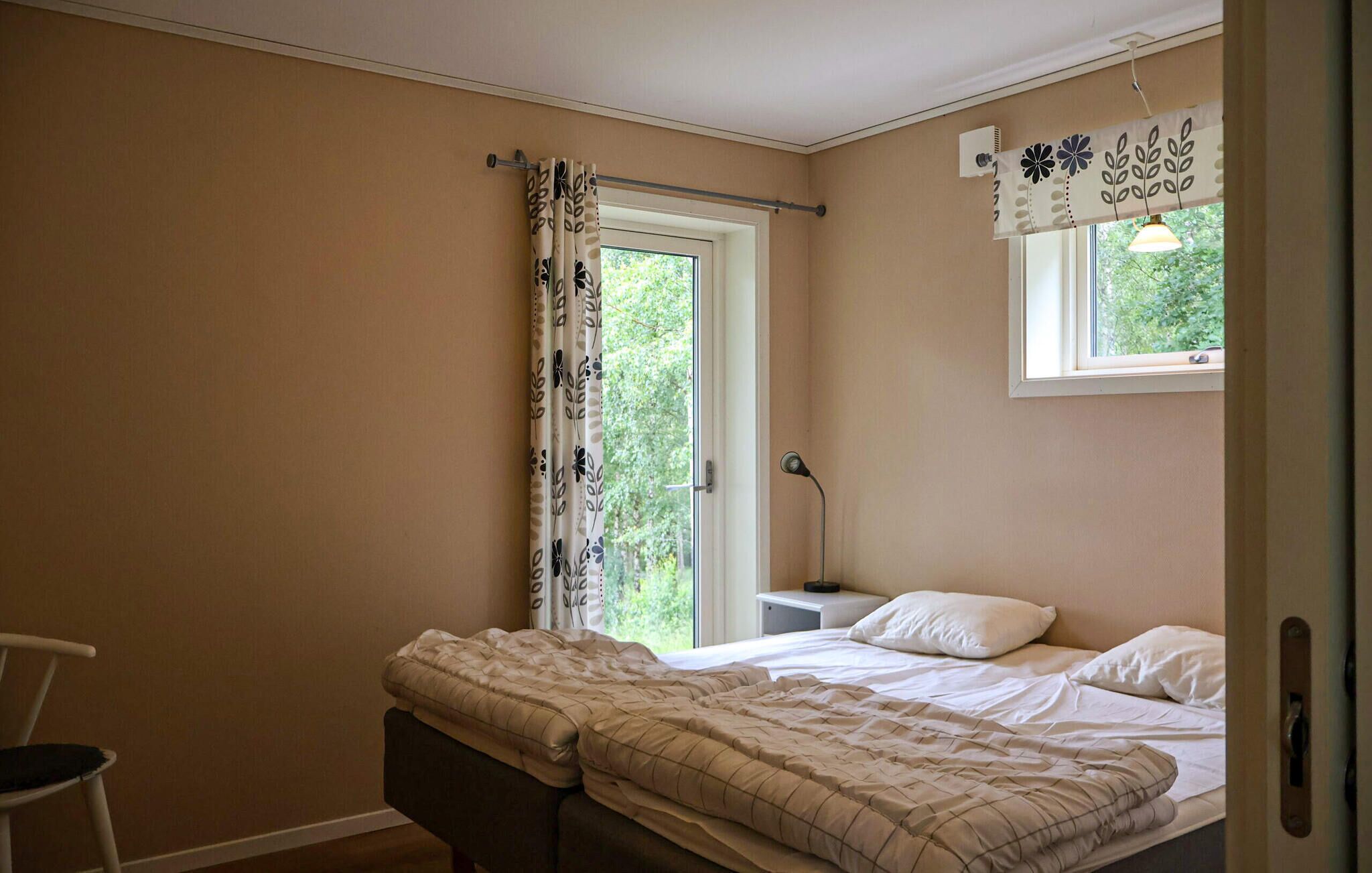 Ein Schlafzimmer mit einem Bett, einem Nachttisch, einem Stuhl, einem Fenster mit Vorhängen und einer Wandleuchte.