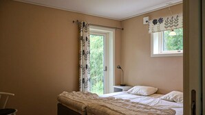 Un dormitorio con una cama, una mesita de noche, una silla, una ventana con cortinas e iluminación fijada a la pared.