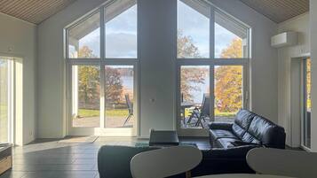 Ein geräumiges Zimmer mit großen Fenstern, einem schwarzen Ledersofa und einem Esstisch.