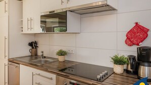 A modern kitchen with white cabinets, a stainless steel range hood, a built-in oven, a sink, and a coffee maker. - Villa Exss Whg. 01 /- - VE 01 (Heringsdorf)
