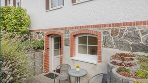 A patio with two chairs and a table, a stone wall, and a small window with a door. - Villa Exss Whg. 01 /- - VE 01 (Heringsdorf)