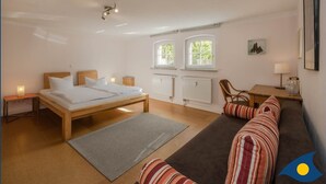 A bedroom with a bed, a sofa, a small table, two windows, and a radiator. - Villa Exss Whg. 01 /- - VE 01 (Heringsdorf)