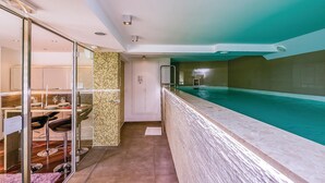 Ein modernes Hotelzimmer mit Glasabtrennung, einem Essbereich mit Barhocker und einem großen Hallenbad.