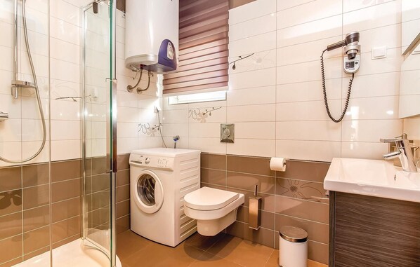 A modern bathroom with a glass-enclosed shower, a built-in washing machine, a toilet, and a sink with a mirror. - Awesome apartment in Crikvenica (Crikvenica)