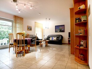 A living room with a dining table, chairs, a sofa, a coffee table, and a bookshelf.