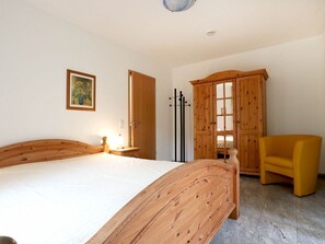 A bedroom with a wooden bed, a yellow armchair, a wooden wardrobe, and a painting on the wall.