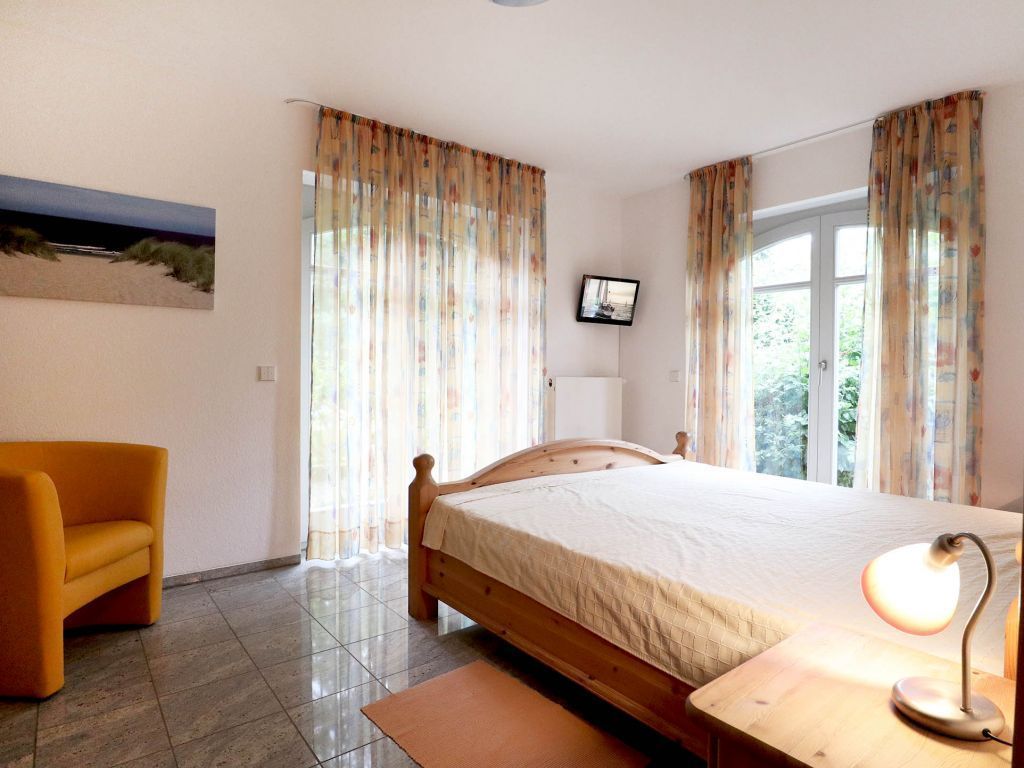 A bedroom with a bed, a chair, a TV, and curtains.