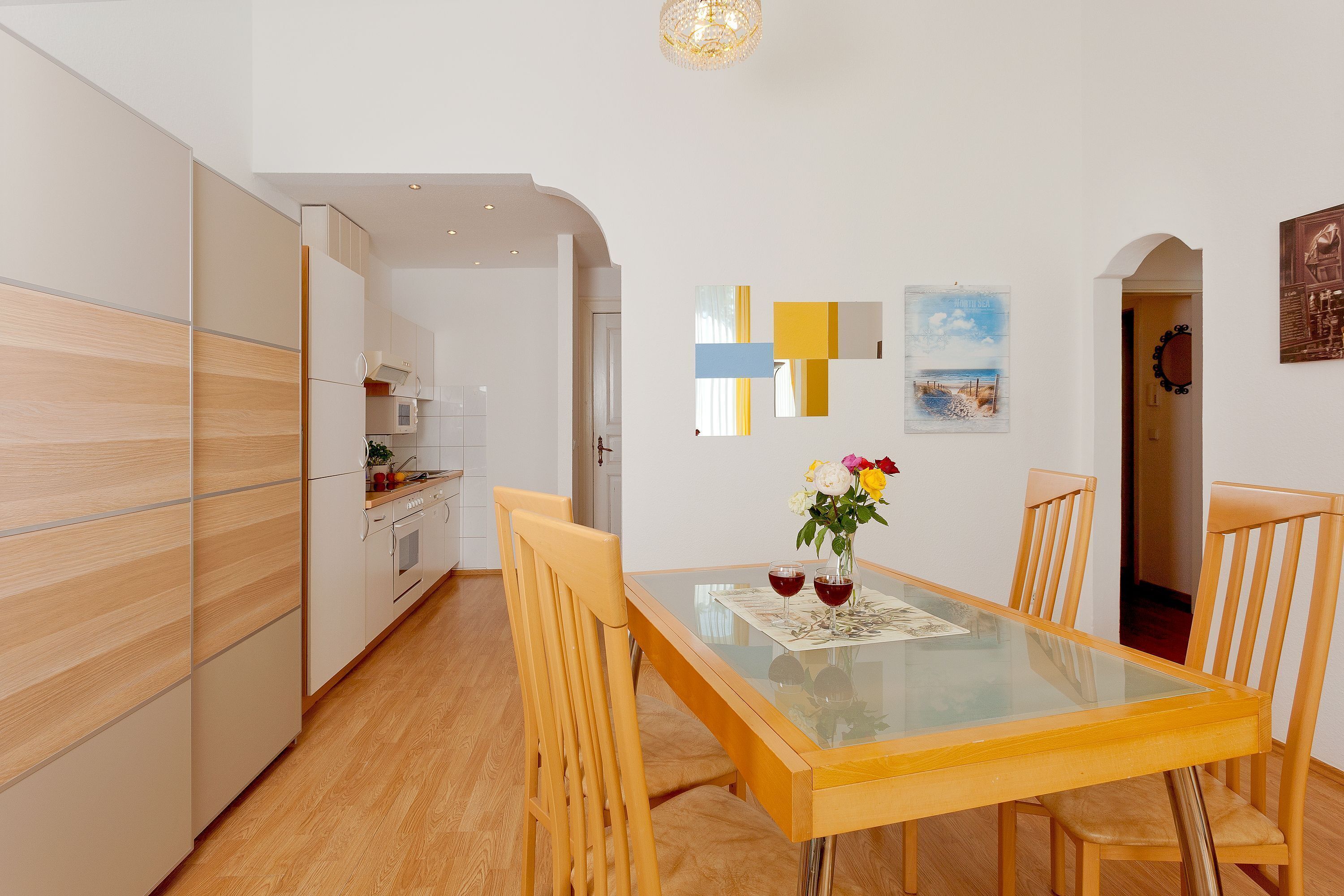 A modern kitchen with white cabinets, a wooden floor, and a dining area with a glass table and wooden chairs.