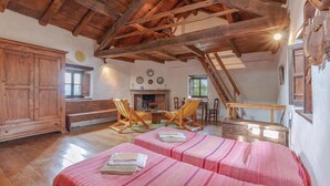 A rustic room with wooden beams, a fireplace, two beds with striped bedding, a wooden bench, and a dining table with chairs. - Awesome home in Borgo Val di Taro PR with WiFi (Borgo Val di Taro PR)