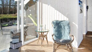 Une pièce dotée d’une porte vitrée donnant sur un espace extérieur, d’un fauteuil en osier, d’une petite table en verre et d’un objet décoratif posé sur le sol.