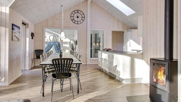 Une salle à manger spacieuse avec une longue table et des chaises, un plafond en bois et une cuisine moderne équipée d’une cuisinière.