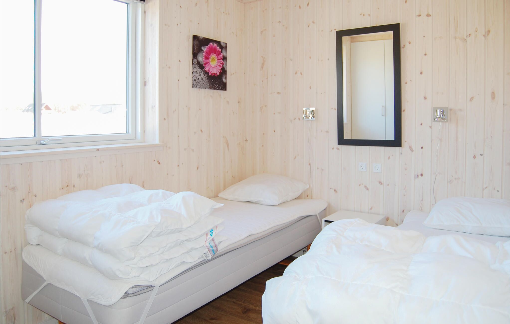 Una habitación con dos camas, una ventana, un espejo y un cuadro colgado en la pared.