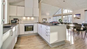 Une cuisine moderne avec des meubles blancs, un four encastré et un coin repas doté d’un plancher en bois et de chaises noires.