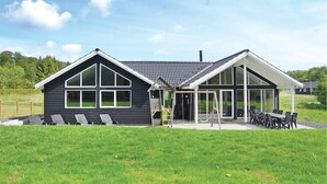 Une maison moderne à deux étages, dotée d’une grande véranda en verre et d’un patio aménagé avec du mobilier d’extérieur.