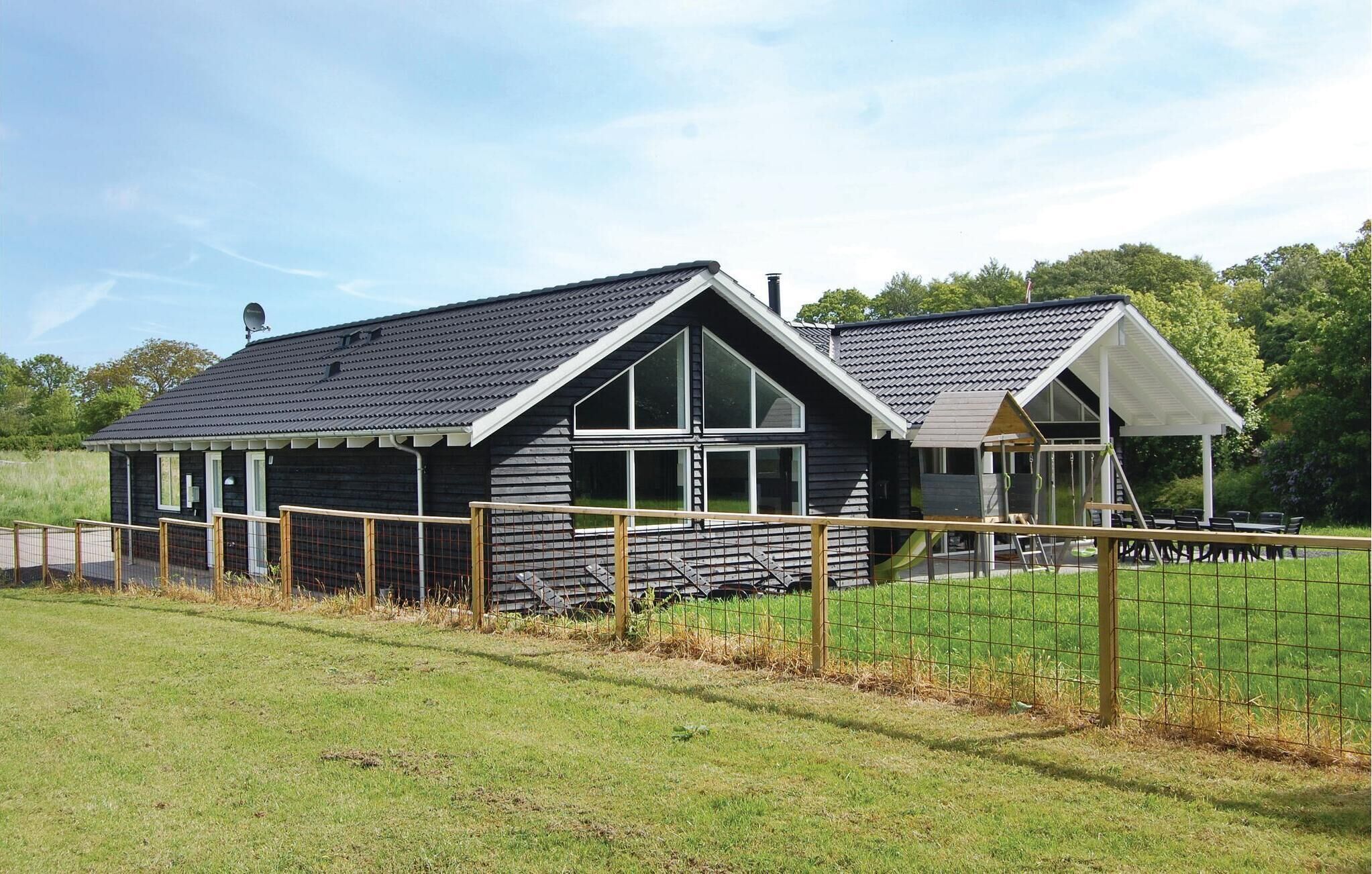 Een modern huis met twee verdiepingen, een schuin dak, grote ramen en een omheinde tuin.