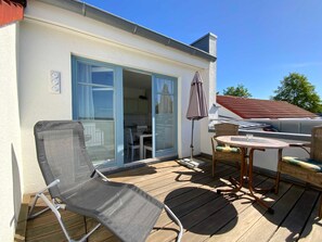 A covered outdoor seating area with a table and chairs, a sliding glass door leading to a kitchen, and a clear blue sky.