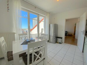 Un comedor con una mesa y sillas, un refrigerador y vistas de una escalera roja en el exterior.