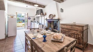 A rustic kitchen with a wooden table set for breakfast, a vintage stove, and a view into the garden.