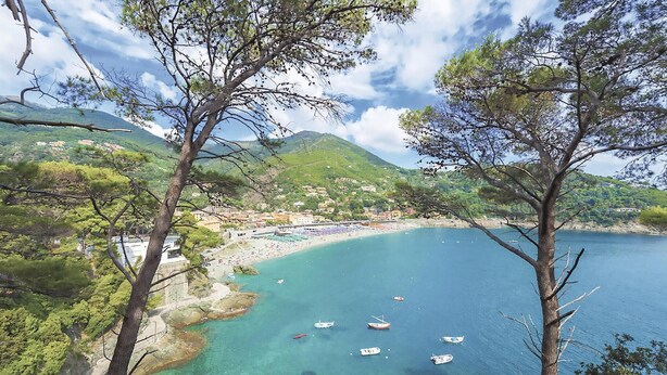 A coastal town with clear turquoise waters, boats, and a mountainous backdrop.