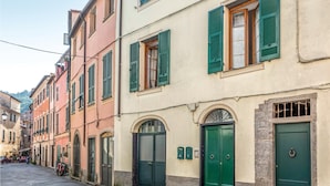 A narrow street lined with colorful buildings, each with green shutters and arched doorways.
