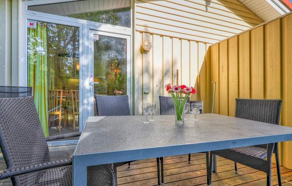 Une terrasse couverte avec une table et des chaises, une porte vitrée et un mur jaune.