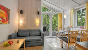 Een gezellige woonkamer met een grijze bank, een houten salontafel en een eethoek met houten stoelen en een tafel.