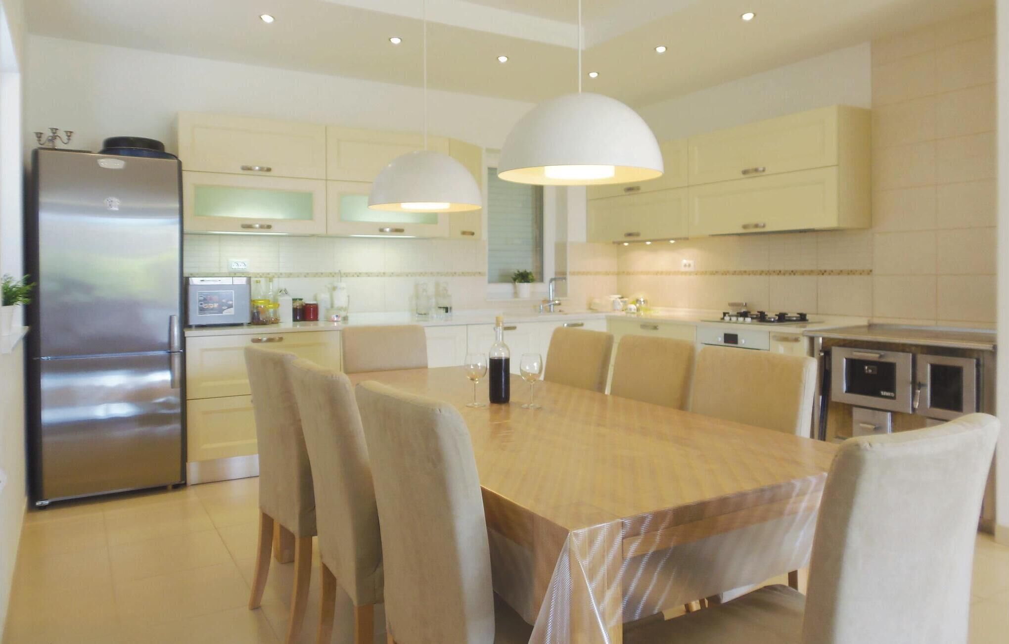 Een moderne keuken met een eethoek, met een grote houten tafel, beige stoelen en roestvrijstalen apparatuur.