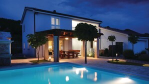 Una casa moderna amb piscina, un pati amb taula i cadires, i un vestíbul ben il·luminat.