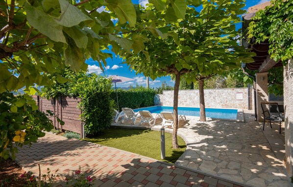 Um quintal com piscina, um muro de pedra e uma cerca de madeira.