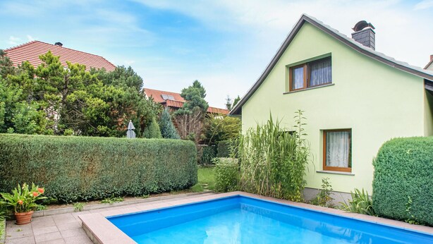 A residential property with a swimming pool, neatly trimmed hedges, and a green building with a sloped roof. - 2 bedroom cozy home in Spitzkunnersdorf (Spitzkunnersdorf)