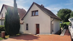 A two-story house with a red-tiled roof, a small front porch, and a driveway leading to a parked car. - 2 bedroom cozy home in Spitzkunnersdorf (Spitzkunnersdorf)